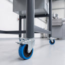 100mm blue braked bolt hole castor fitted to a steel machine stand leg in a factory