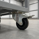 100mm braked top plate castor with black rubber wheel bolted under a grey steel warehouse trolley