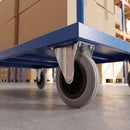 100mm fixed castor with grey rubber wheel bolted under a blue warehouse platform trolley loaded with boxes