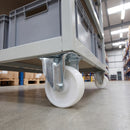 100mm fixed castor white nylon wheel bolted under a grey warehouse trolley with tote boxes