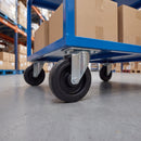100mm fixed top plate castor with black rubber wheel under a blue steel warehouse trolley loaded with boxes