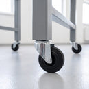 100mm black rubber bolt hole castors on a grey steel machine stand in a manufacturing hall