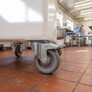 160mm braked top plate castor with grey TPR wheel under a white dough tub dolly on a quarry-tiled food factory floor