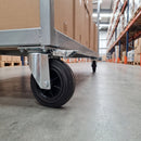160mm directional lock castor with black rubber wheel under a galvanised warehouse trolley in a racking aisle