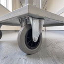 160mm fixed top plate castor with grey ribbed rubber wheel bolted under a grey steel trolley in a hospital corridor