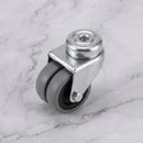 50mm twin wheel swivel bolt hole castor with grey rubber wheels on light grey marble, 45 degree three-quarter view from a steep high angle