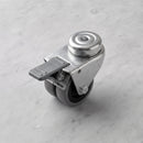 75mm twin wheel braked bolt hole castor with grey rubber wheels and grey foot brake on light grey marble, 45 degree three-quarter view from a steep high angle