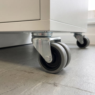 75mm twin wheel top plate castor with grey rubber wheels fitted under a white mobile storage cabinet