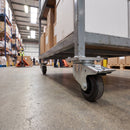 80mm braked castor with black rubber wheel under a grey steel warehouse trolley loaded with boxes