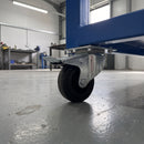 80mm braked top plate castor with black rubber wheel fitted under a blue steel machine stand in a workshop