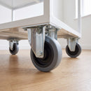 80mm fixed top plate castor with grey rubber wheel bolted under a white office storage trolley on laminate flooring
