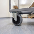 80mm fixed top plate castor with grey rubber wheel fitted under a grey steel stockroom trolley on vinyl flooring