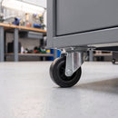 80mm swivel castor with black rubber wheel bolted under a grey steel drawer unit in a workshop