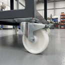 Braked swivel castor with white nylon wheel bolted under a grey workshop trolley