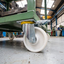 Directional lock castor with white nylon wheel bolted under a green industrial cart carrying steel parts