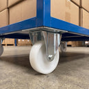 Fixed castor with white nylon wheel fitted under a blue warehouse trolley